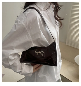 Close-up of dark burgundy patent leather shoulder bag with gold metal bow buckle detail