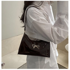 Detail of dark brown patent leather shoulder bag with a gold metal bow ornament