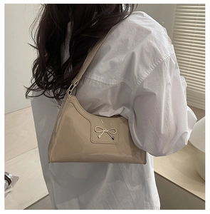 Detail of a cream patent leather shoulder bag with a gold bow accent on a model