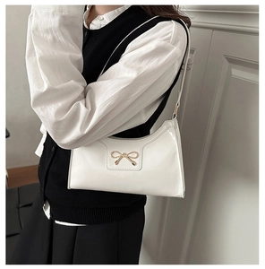 Detail of white patent leather shoulder bag featuring a metallic gold bow and slim strap