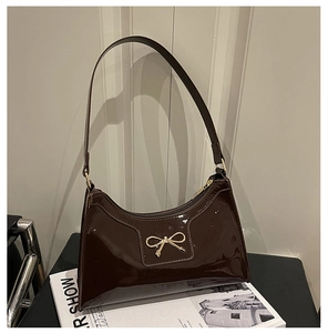Detail of dark brown patent leather handbag with gold bow buckle on a fashion magazine