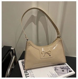 Detailed shot of glossy beige patent leather bag with gold bow clasp on a magazine