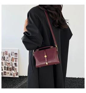 Detail of burgundy leather crossbody bag with gold ring buckle on model's black coat