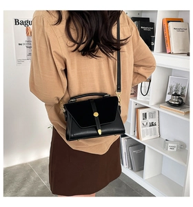 Detail of a black PU leather crossbody bag with suede patchwork and gold buckle on a model