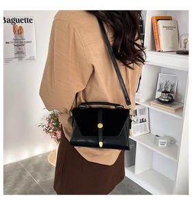 Detail of a black PU leather crossbody bag with a gold buckle worn by a model