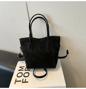 Detail of black suede tote bag featuring cylindrical handles and adjustable strap hooks