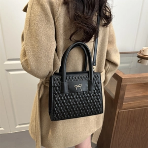 Quilted black leather handbag with a gold bow accent and detachable shoulder strap