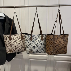 Three monogrammed tote bags in beige, blue, and brown hanging on a metal display rack