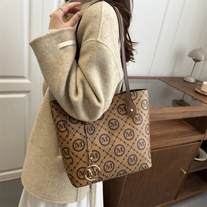 Classic brown leather tote bag with monogram print and metal M-pendant worn by a woman