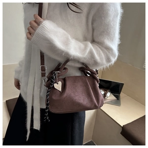 Détail du sac à main en daim marron foncé avec poignée tressée et breloque en cœur