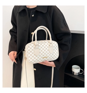 Détail du sac Boston crème avec motif de chaîne rétro et logo doré porté par un mannequin