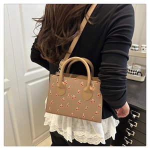 Detail view of small beige cherry print square bag worn by model in cozy home setting