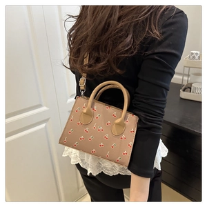 Detail view of beige crossbody bag with red cherry print worn by a model in casual setting
