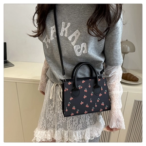 Detailed view of black tote bag featuring red cherry prints with long shoulder strap
