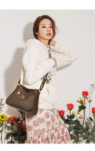 Detail of dark brown leather shoulder bag featuring a gold kangaroo logo and strap