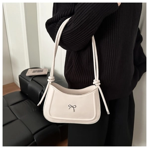 Detail of minimalist cream leather shoulder bag with a silver metallic bow and knot handle