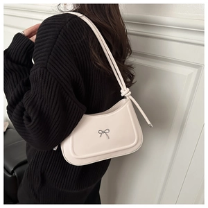 Close-up of minimalist cream white shoulder bag featuring a silver bow buckle and knot strap