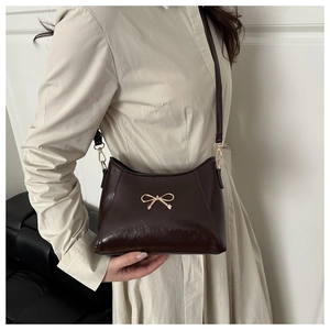 Detail of dark brown glossy wrinkled leather shoulder bag with a gold bow buckle accessory