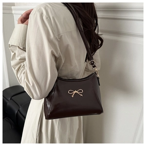 Detail of burgundy patent leather handbag featuring a golden bow buckle and strap