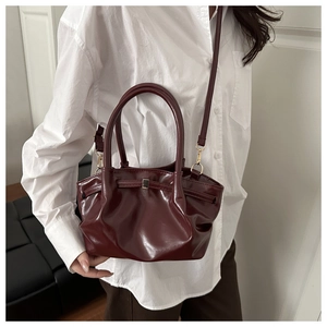 Detail of burgundy glossy pleated bucket bag with adjustable strap on white shirt