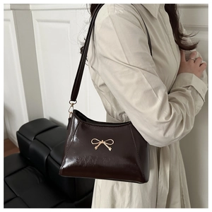 Close-up of brown patent leather handbag featuring a golden bow metal accessory and strap