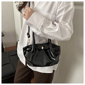 Detail of black pleated tote bag showing glossy texture and golden metal buckle