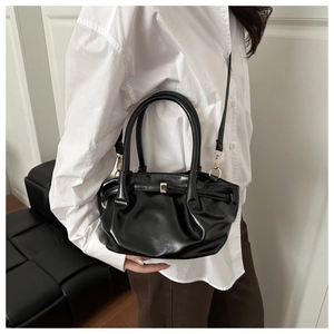 Detail of black glossy bucket bag with pleated design and gold buckle worn by model