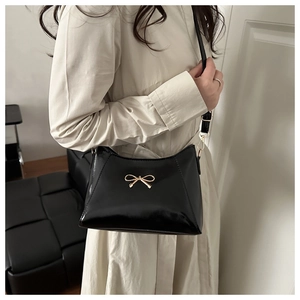Detail of a black glossy shoulder bag featuring a golden bow metal accessory and strap
