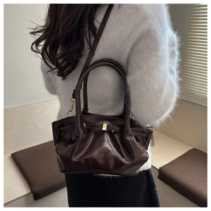 Detailed side view of dark brown glossy bucket bag with pleated texture and gold buckle