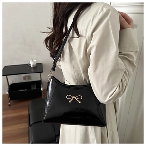 Close-up of black glossy PU leather shoulder bag featuring a gold bow metal hardware detail