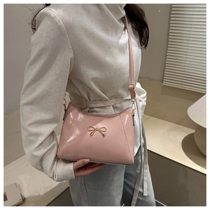 Close-up of pink glossy shoulder bag with golden bow decoration worn by model