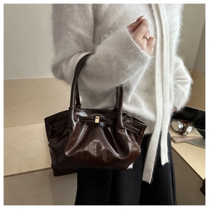 Detail of a dark brown glossy patent leather bucket bag with a gold buckle on a sweater