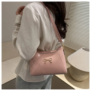 Pink PU leather shoulder bag with gold bow buckle shown on a model in a warm room