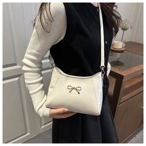 Detail of cream-colored crossbody bag featuring textured leather and a golden metal bow