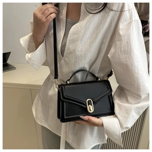 Detail van een zwarte crossbodytas met een gouden draaisluiting en een stijlvolle flap