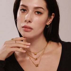 Gouden drielaagse ketting met cilindervormige hangers en gedraaide oorbellen op model