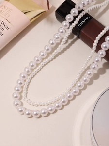Colliers de perles blanches superposés avec fermoir métallique sur fond neutre