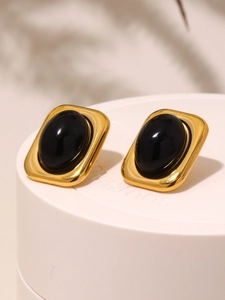Nahaufnahme von Vintage-Goldohrringen mit ovalem schwarzem Onyx auf weißem Podest