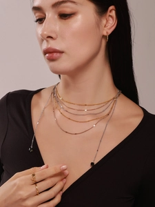 Close-up of layered gold chain necklace with dark stone beads and flower relief rings