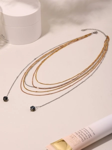 Detail of layered gold and silver chain necklace with dark blue diamond beads