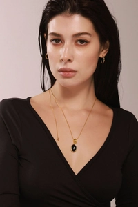 Détail d'un collier pendentif pierre noire ovale avec des boucles d'oreilles dorées