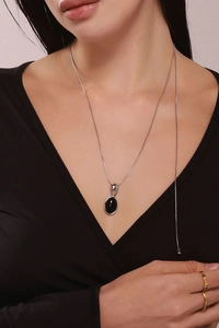 Détail du collier chaîne serpent argentée avec pendentif ovale noir et bague dorée ondulée