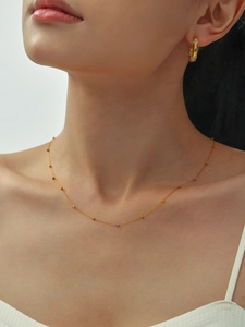 Detalle del collar de cuentas minimalista chapado en oro y pendientes de aro con cristales