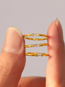 Close-up of three gold rings featuring rectangular white zircon stones on a model's hand
