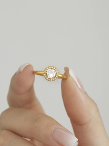 Detail of a thin gold ring featuring a sparkling round zircon halo setting held by hand