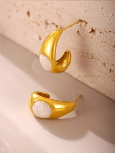 Gros plan de boucles d'oreilles dorées en C avec émail rose sur fond de pierre