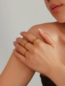 Detail of three stacked gold rings set with green cubic zirconia on a model's hand