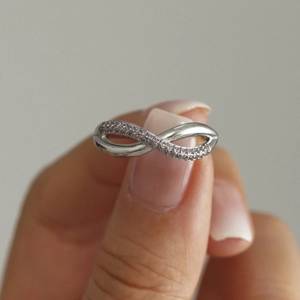 Silver infinity ring with pink cubic zirconia stones shown on hand for women