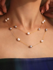 Detailed close-up of double-layer gold chain necklace with baroque pearls on a model
