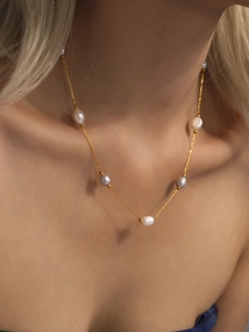 Detail of elegant gold chain necklace with natural baroque pearls on female neck and collarbone